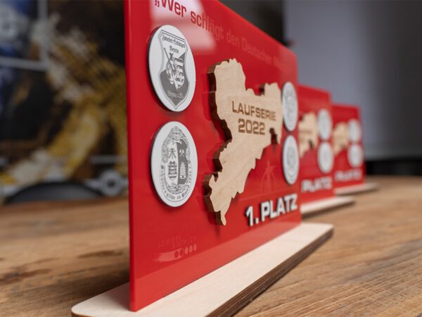 Pokal aus verschiedenen Materialien wie hier rotes Acryl, Speerholz, silber-schwarzes Lasermexx. Alle Mverwendeten Materialien sind zusätzlich graviert.