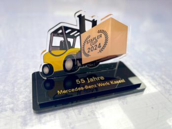 Pokal für einen Gabelstaplercup aus transparentem bedruckten Acryl und schwarzem Acryl. Der Schriftzug aus gelasertem dünnen Lasermexx ist als Einzelbuchstaben auf die schwarze Grundplatte geklebt
